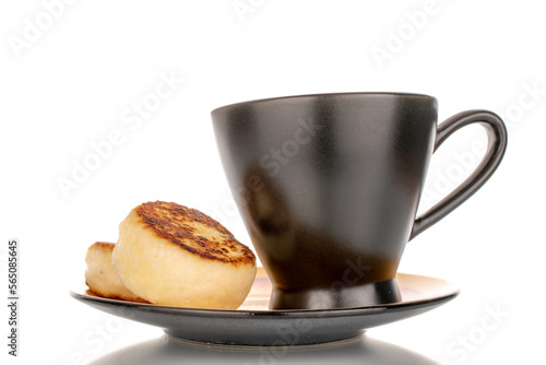 Fototapeta Naklejka Na Ścianę i Meble -  Two homemade cheese pancakes on a black ceramic saucer with a black cup, macro, isolated on white background.
