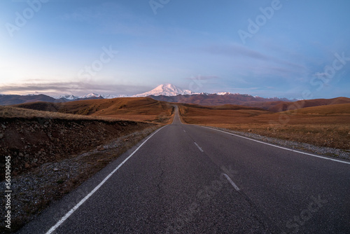Morning highway to the snow-capped peaks. Autumn morning deserted highway. Beautiful asphalt freeway, motorway, highway through of caucasian landscape mountains hills.
