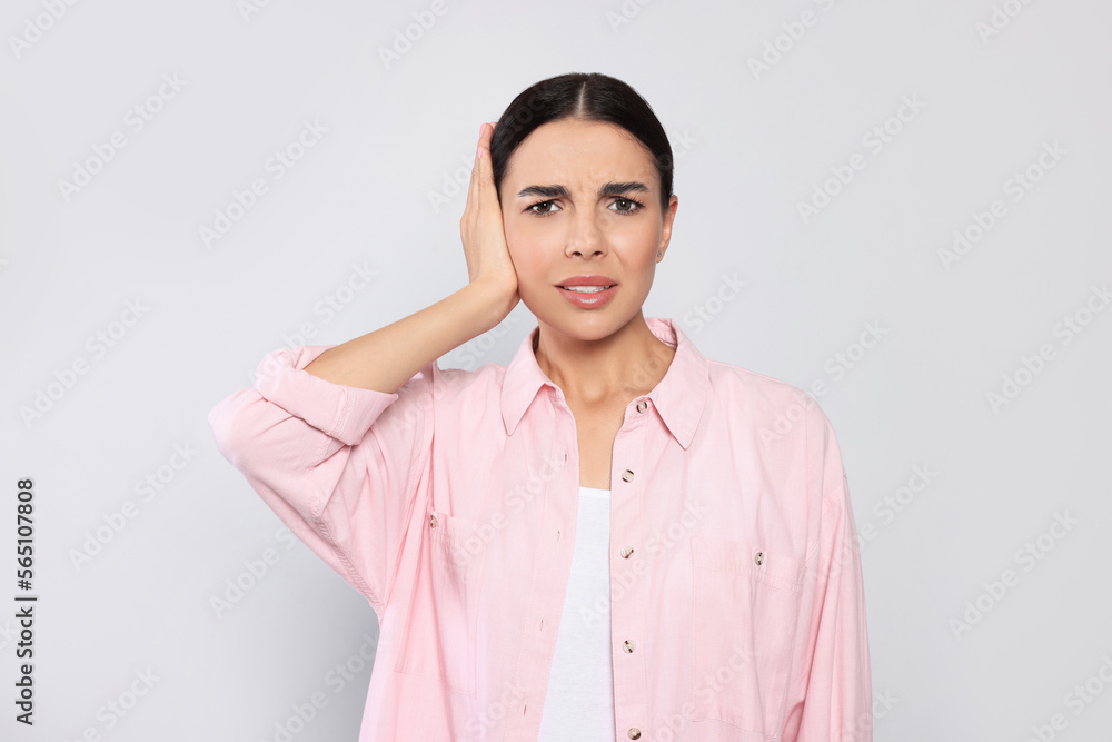 Young woman suffering from ear pain on light grey background Young woman suffering from ear pain on light grey background