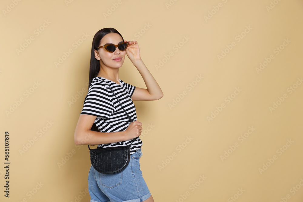 Beautiful young woman with stylish bag in sunglasses on beige background, space for text Beautiful young woman with stylish bag in sunglasses on beige background, space for text