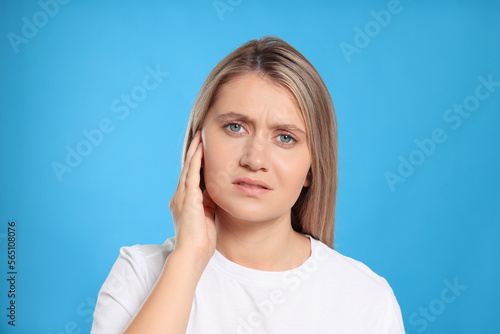 Young woman suffering from ear pain on light blue background