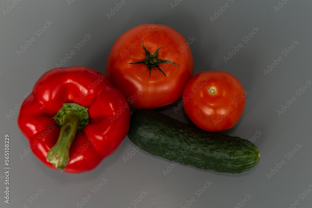 Ripe and beautiful red bell pepper, green cucumber and two tomatoes on a gray background. Vegetarian food. Close-up.