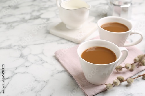 Cups of hot aromatic coffee and willow branches on white marble table. Space for text