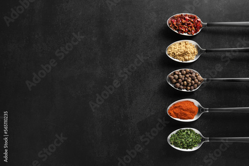 Metal spoons with different spices on black table, flat lay. Space for text