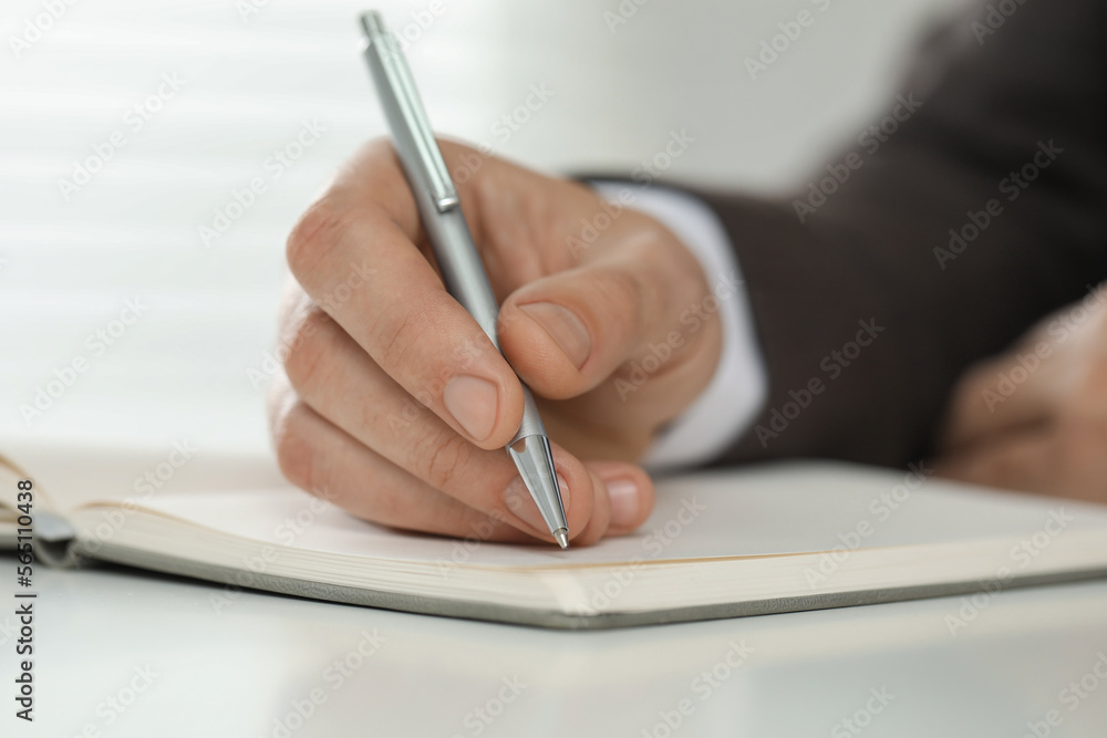 Man writing in notebook at white table, closeup Man writing in notebook at white table, closeup