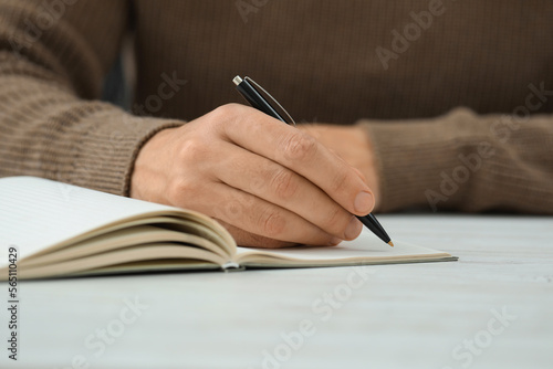 Man writing in notebook at white table, closeup