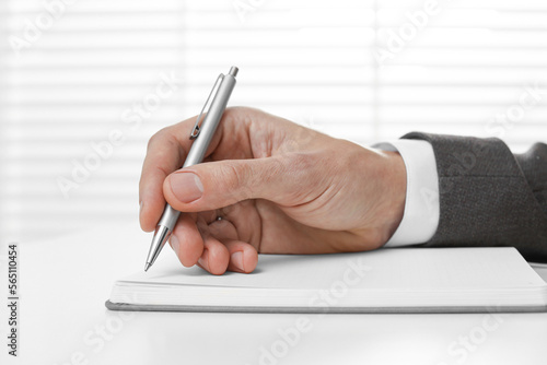 Man writing in notebook at white table, closeup