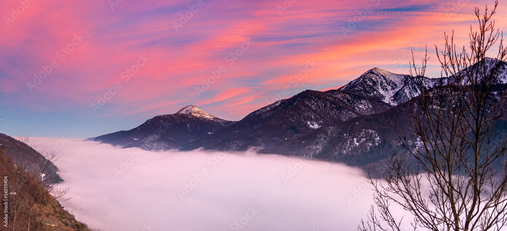 Glorious sunset in the italian Alps. Beautiful sky over misty valley and snowcapped mountain peaks. Winter in Piedmont, Italy.