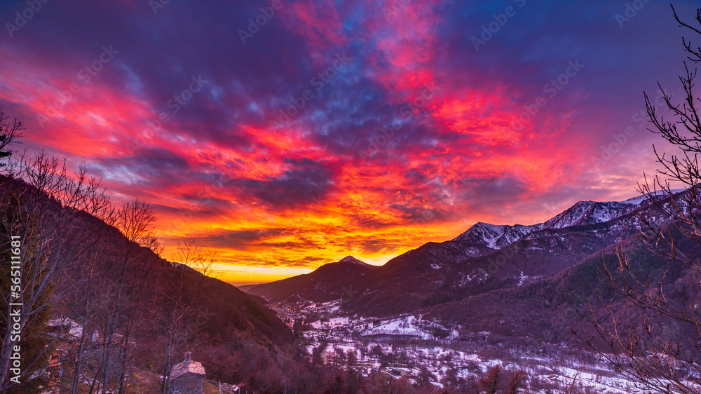 Glorious sunset in the italian Alps. Beautiful sky over snowy valley idyllic village and snowcapped mountain peaks. Winter in Piedmont, Italy.