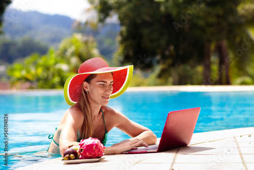 Woman with laptop at swimming pool. Remote work.