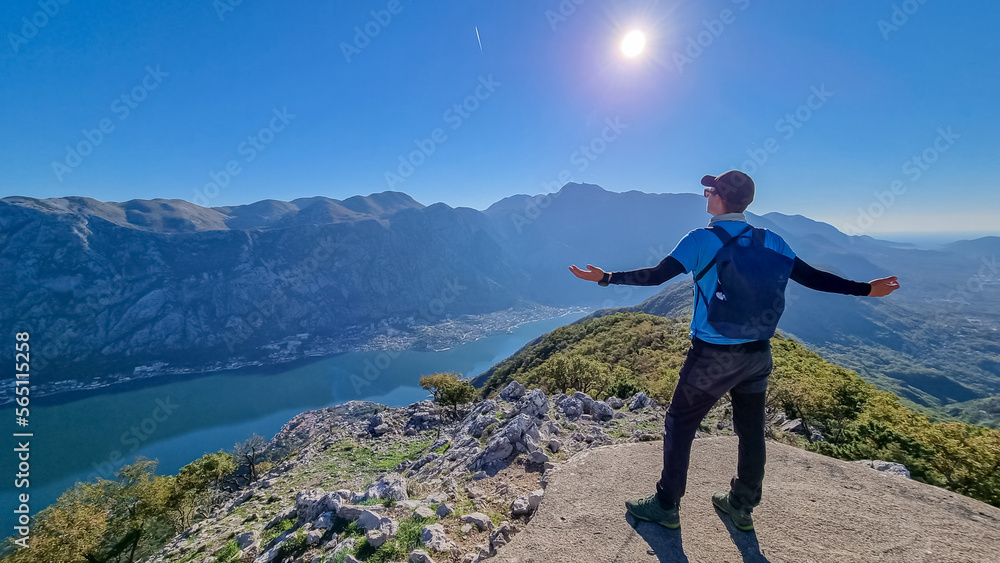 Man with scenic view from mountain summit of Vrmac Sveti Ilija on Kotor bay in summer, Adriatic Mediterranean Sea, Montenegro, Balkans, Europe. Fjord winding along coastal towns. Hiking Dinaric Alps