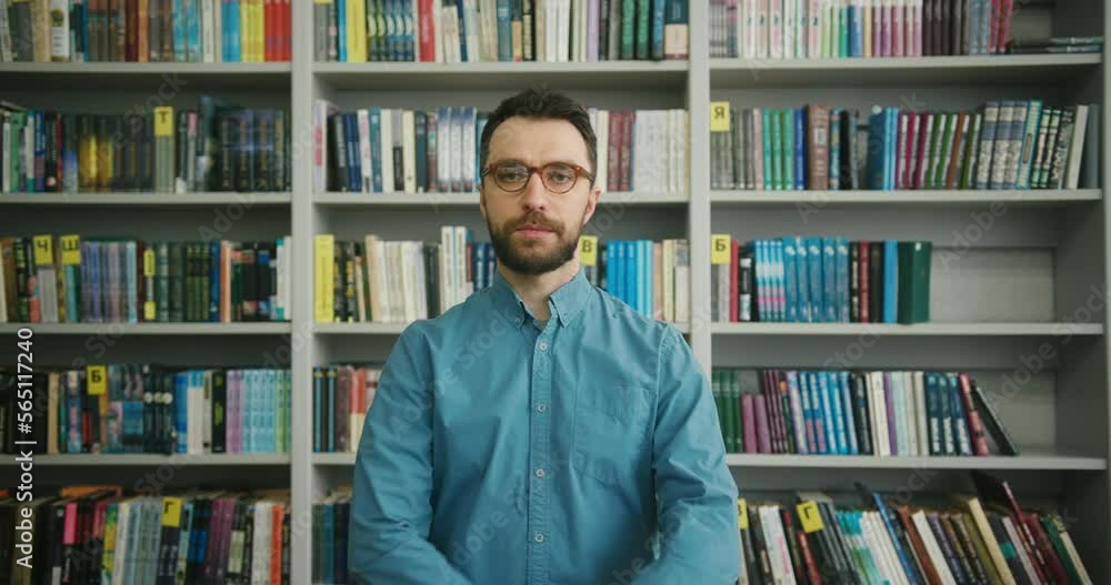 Bearded man stands against racks with books in library Bearded man stands against racks with books in library