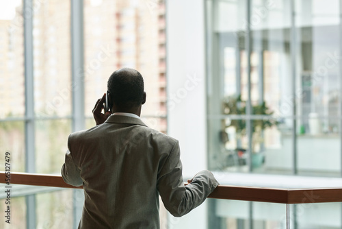 Back view of experienced African American male chief executive officer talking on mobile phone while standing by railing in office center
