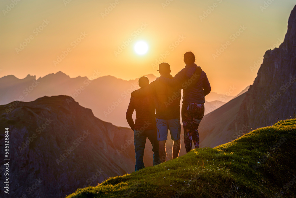 3 friends hugging each other looking at sunset in the mountains