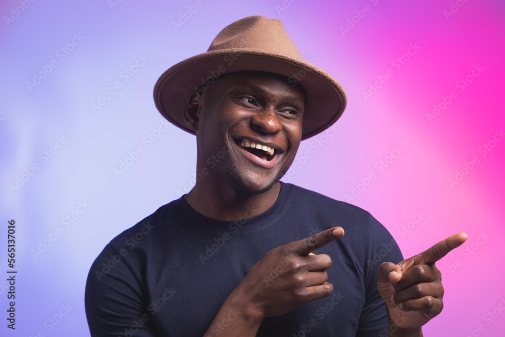 Young amazed African American looking with opened mouth showing teeth, pointing his finger at background Young amazed African American looking with opened mouth showing teeth, pointing his finger at background