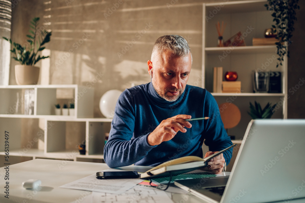 Middle aged man working in a home office and using laptop and taking notes Middle aged man working in a home office and using laptop and taking notes