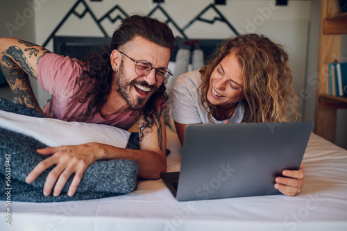 Romantic couple lying in the bed at home in the morning and using laptop