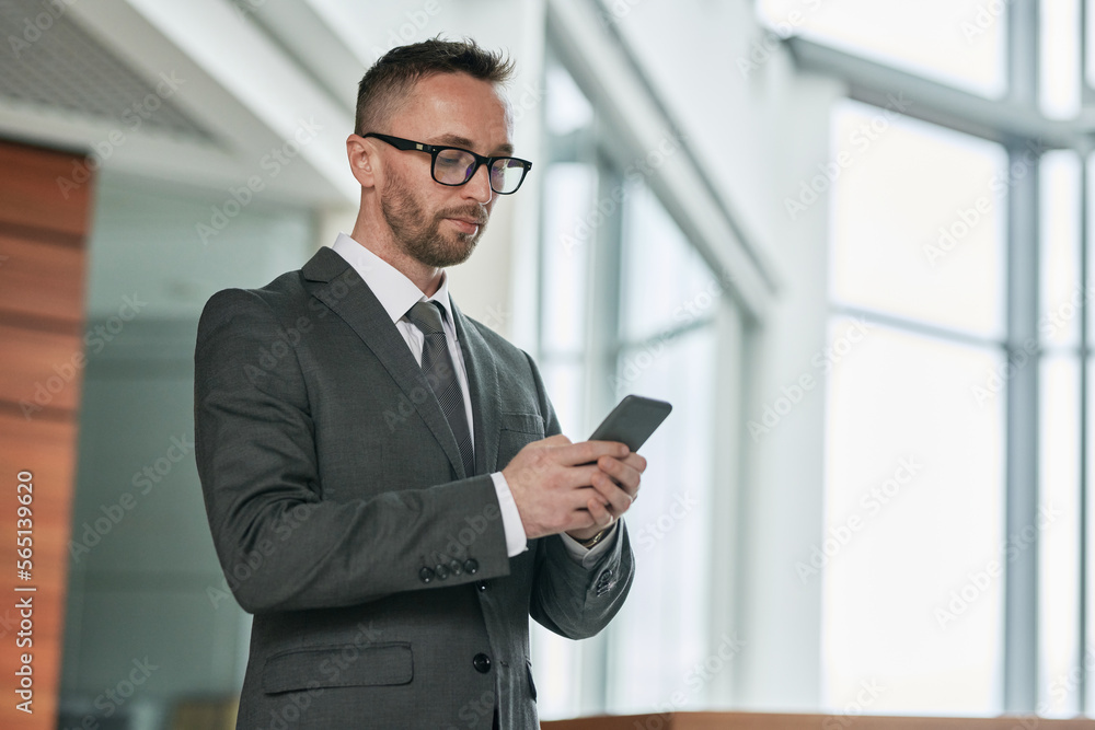 Young serious male broker in formalwear texting in mobile phone while communicating with colleague or client inside office center Young serious male broker in formalwear texting in mobile phone while communicating with colleague or client inside office center