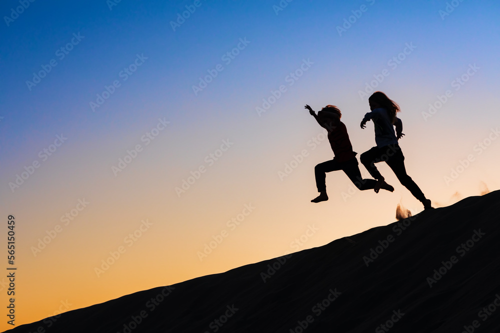 Black silhouette at sunset sky background. Happy family - kids running and jumping high in the air from sea beach sand dune. Active people, outdoor activity on tropical summer vacations with children