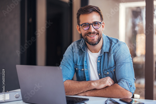 Fotografiet Portrait of attractive smiling man sitting in office and looking at camera