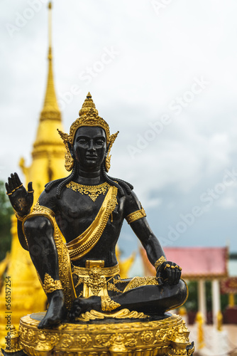A black and golden buddha statue at a temple with a stuppa in the background 