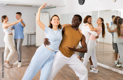 Joyful young adult couples learning passionate pair dancing during practicing in choreography class