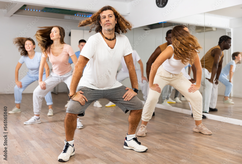 Big group of young adult fit people in activewear exercising together during training in dance studio