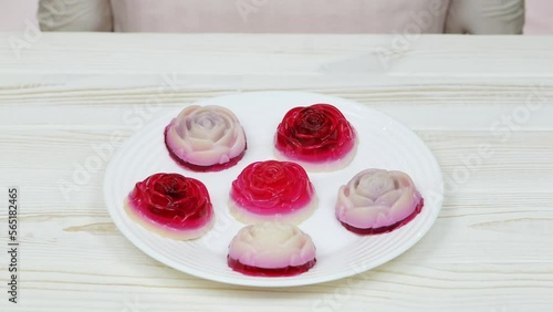 Rose shaped jelly dessert made from raspberries and cream in a white plate on a white wooden table. The chef puts a plate of dessert on the table.