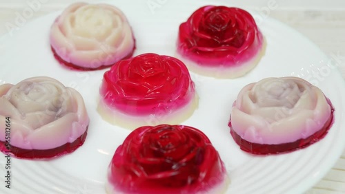 Rose shaped jelly dessert made from raspberries and cream in a white plate on a white wooden table.