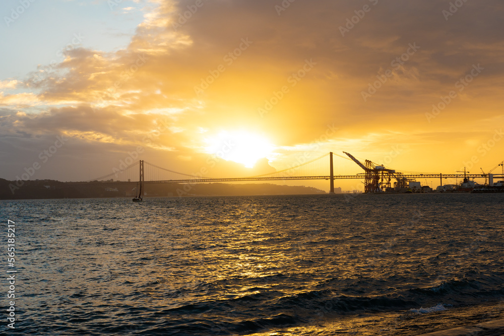 Sunset over the sea and silhouettes of a bridge and an industrial crane
