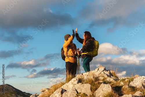 Couple of mountaineering hikers  with backpack and trekking poles  high-fiving as they reach the top of a mountain. Outdoor sports and weekend activities.