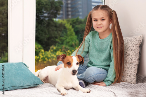 Cute girl with her dog on window sill indoors. Adorable pet © New Africa