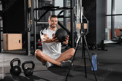 Man with ball streaming online training on phone at gym. Fitness coach