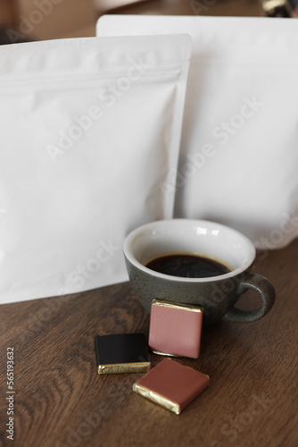 Cup of aromatic coffee, packages with beans and chocolate on wooden table indoors