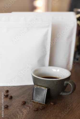 Cup of aromatic coffee, packages with beans and chocolate on wooden table indoors