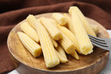 Pickled baby corn and fork on white wooden table, closeup
