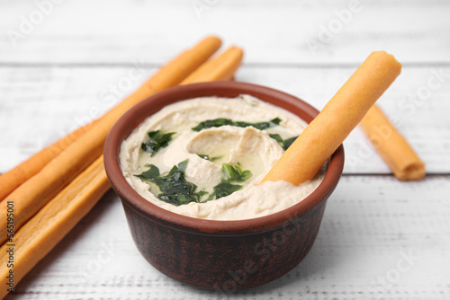 Delicious hummus with grissini sticks on white wooden table