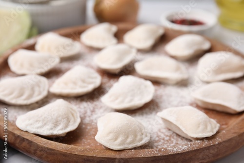 Raw dumplings (varenyky) with tasty filling and flour on wooden board, closeup