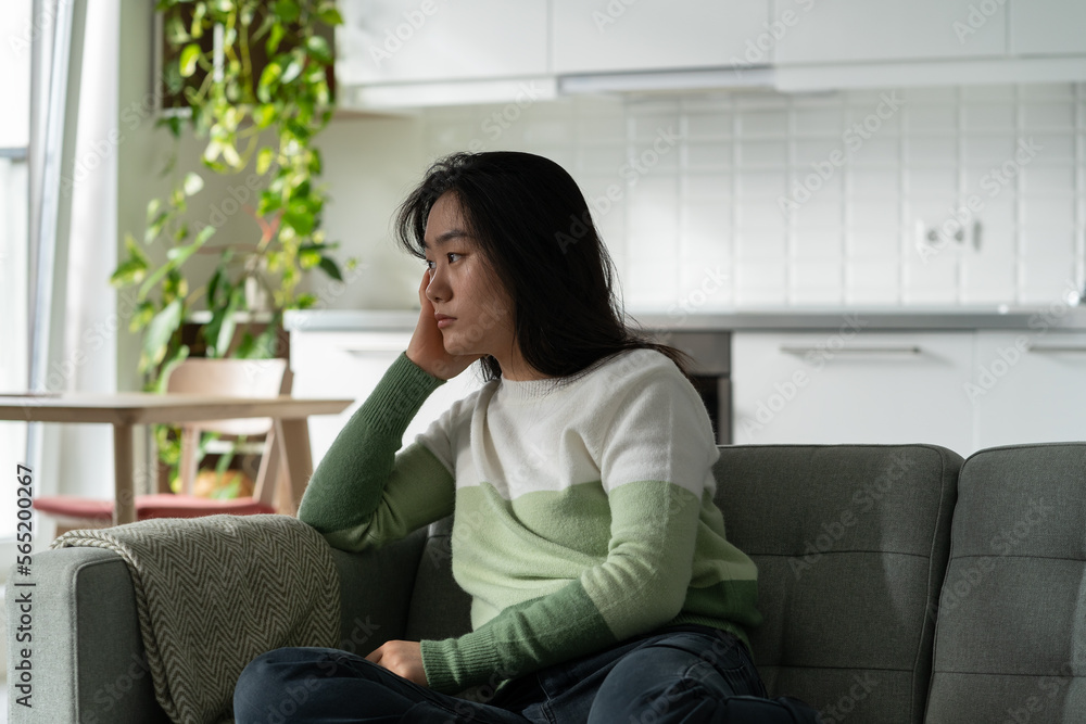 Anxious Asian millennial girl sitting on sofa feeling lonely, suffering from monophobia. Sad depressed young Korean woman sits alone at home looking aside, having problems dealing with panic attack Anxious Asian millennial girl sitting on sofa feeling lonely, suffering from monophobia. Sad depressed young Korean woman sits alone at home looking aside, having problems dealing with panic attack