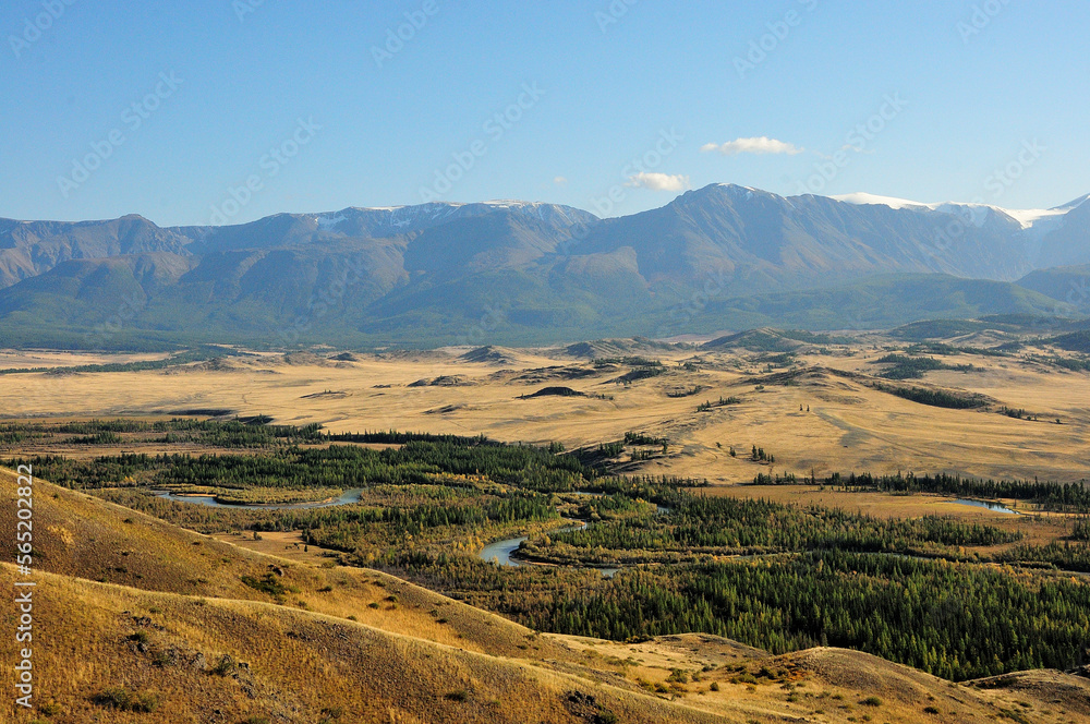 High mountains on the edge of the steppe and a winding river flowing through the valley on a sunny autumn evening. High mountains on the edge of the steppe and a winding river flowing through the valley on a sunny autumn evening.