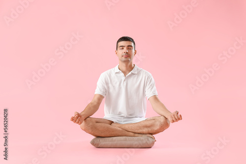Young man meditating on pink background