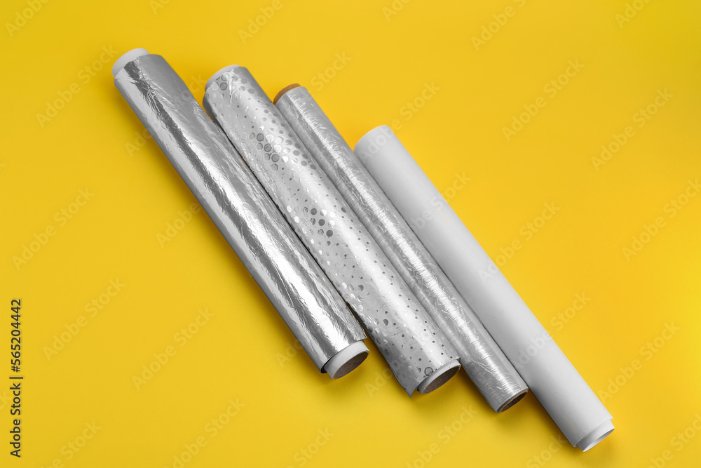 Naklejka premium Rolls of aluminium foil, baking paper and food film on yellow background