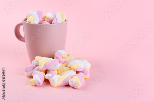 Cup with tasty twisted marshmallows on pink background