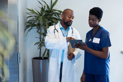African american male and female doctor looking at tablet in hospital corridor with copy space