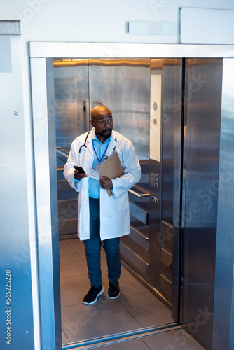 Vertical of african american male doctor using smartphone in hospital lift with copy space