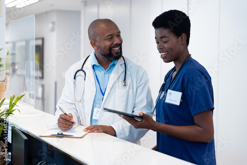 Smiling african american male and female doctor with tablet talking in hospital corridor