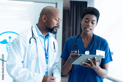 African american male and female doctor using tablet, talking in hospital with copy space