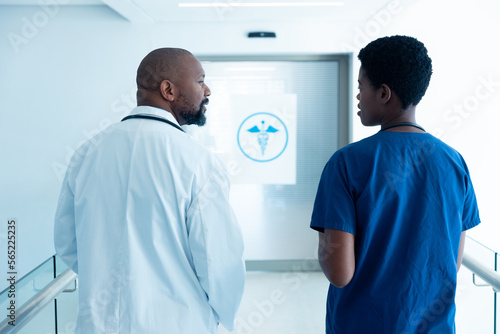Rear view of african american male and female doctor talking in hospital corridor with copy space