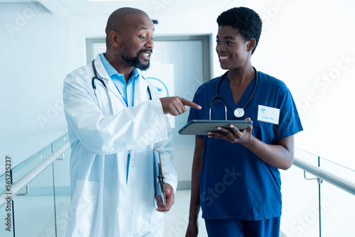 Smiling african american male and female doctor using tablet, talking in hospital with copy space