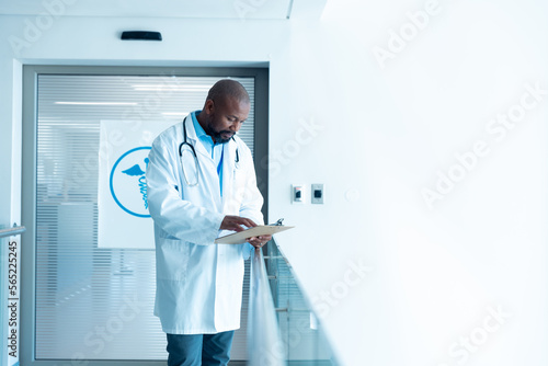 Serious african american male doctor reading notes in hospital corridor with copy space